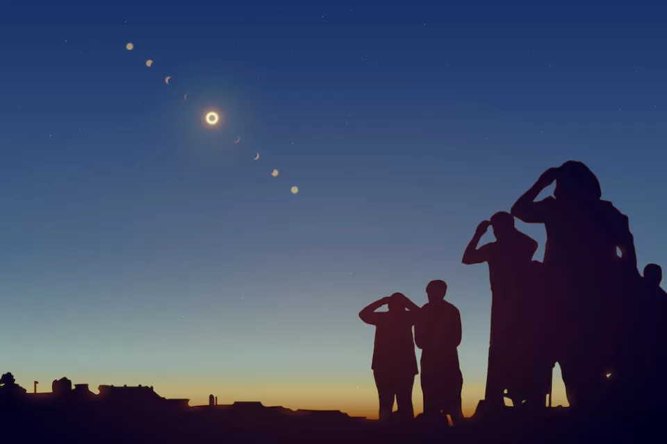 Sillhouettes of group of people watching solar eclipse.